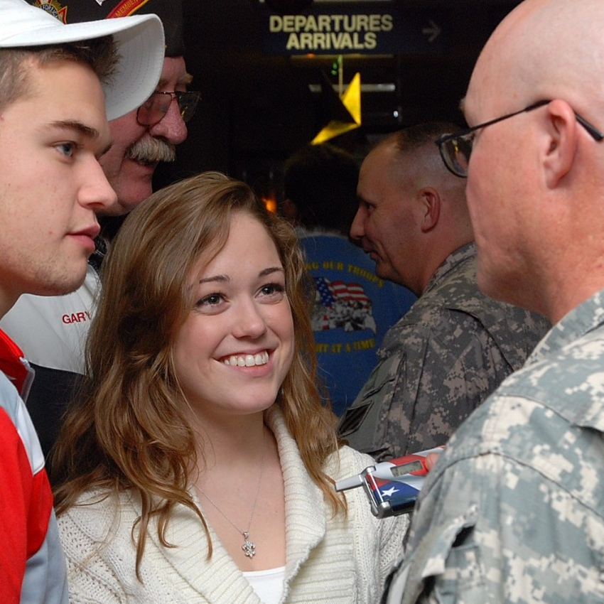 Brittany and Robbie Bergquist engaging in conversation with a military service member at an airport.